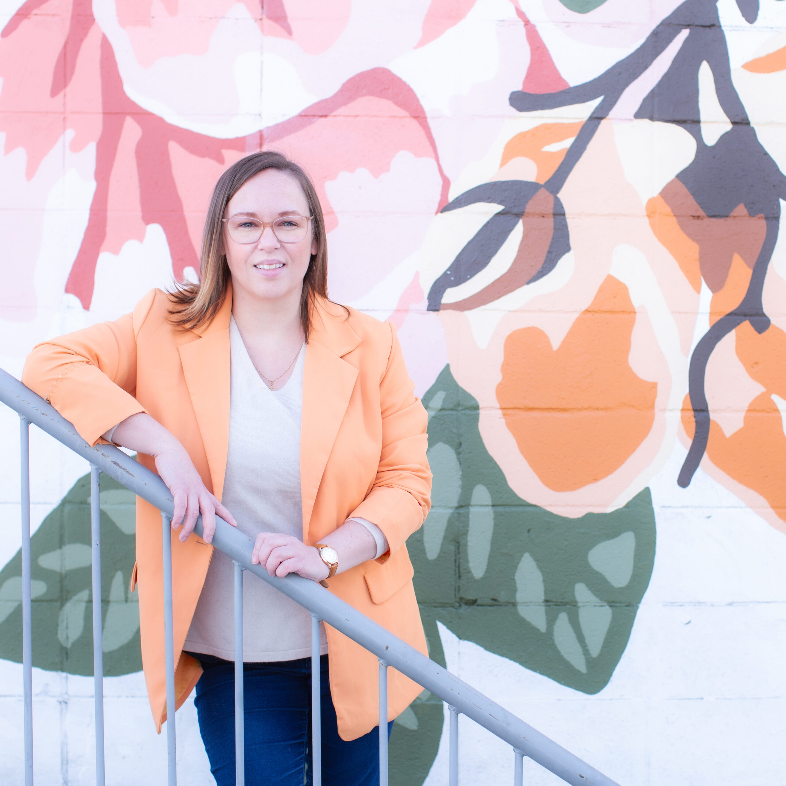 Amanda Wall, multi-disciplinary artist, standing in front of a vibrant floral mural
