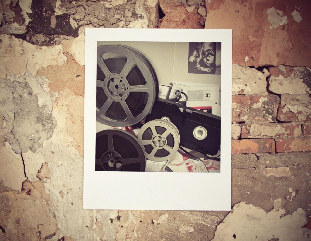 Old film projector and polaroid photo on a textured wall, symbolizing pop culture and media history.