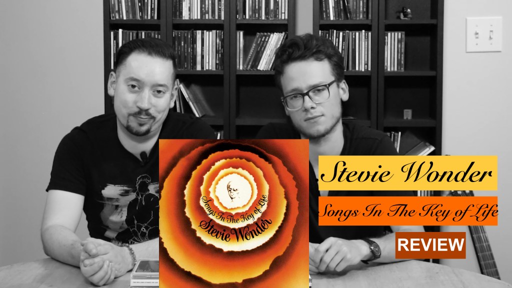 timotheories and Dont Bartlett sit at a table with Songs in the Key of Life by Stevie Wonder prominently displayed, teasing an upcoming YouTube video on the essential album.