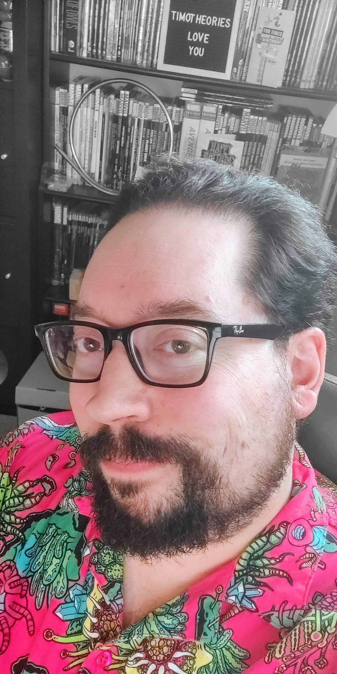Tim Kuefler smiling in front of a bookshelf, wearing a colorful shirt and glasses — founder of timotheories